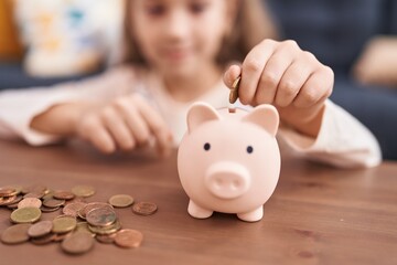 Adorable caucasian girl inserting coin on piggy bank sitting on sofa at home