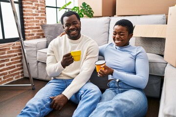 Man and woman couple drinking coffee sitting on floor at new home