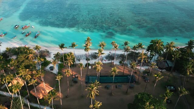 Cinematic aerial view palm trees along beach with white sand and turquoise sea on on the territory of a luxury hotel with a swimming pool. Summer vacations concept in tropical resort