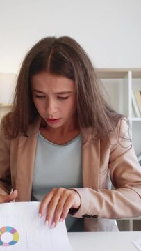 Vertical video. Report presentation. Nervous work. Online interview. Anxious stressed scared woman in business suit looking for papers on table in office.