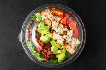 Plastic package with healthy cobb salad with chicken, avocado, bacon, blue cheese, tomatoes and eggs to take away