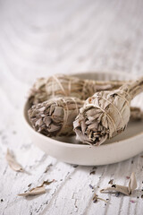 Smudge sticks with White Sage (Salvia apiana) in a white bowl on old white wooden table