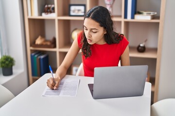 Young african american woman using laptop writing on document sitting on table at home