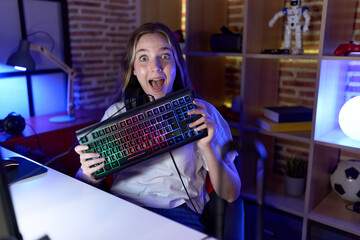 Young caucasian woman holding gamer keyboard celebrating crazy and amazed for success with open eyes screaming excited.