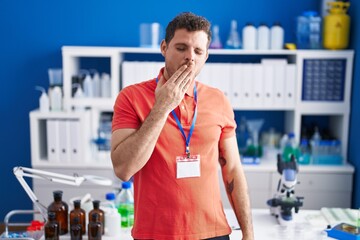Young hispanic man working at scientist laboratory bored yawning tired covering mouth with hand....