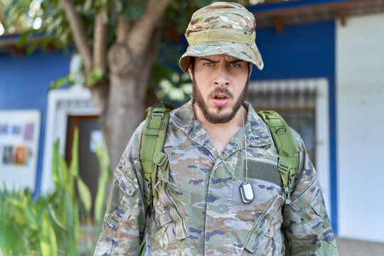 Young hispanic man wearing camouflage army uniform outdoors scared and amazed with open mouth for surprise, disbelief face