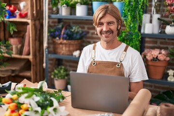 Young blond man florist smiling confident using laptop at flower shop