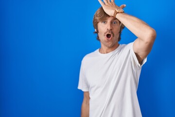Naklejka premium Middle age man standing over blue background surprised with hand on head for mistake, remember error. forgot, bad memory concept.