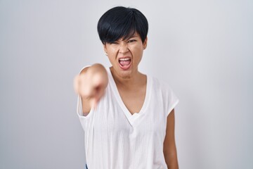 Young asian woman with short hair standing over isolated background pointing displeased and...