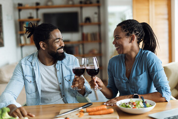 Happy African American couple toasting with wine during lunch at dining table