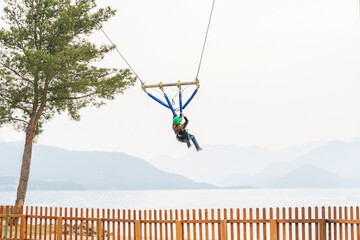 Teenage teen girl bungee flying in rope amusement park. Climbing harness equipment, green sports...