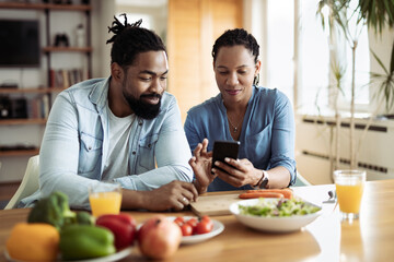 Fototapeta na wymiar Happy African American couple using a phone while having breakfast in the morning.Focus is on woman