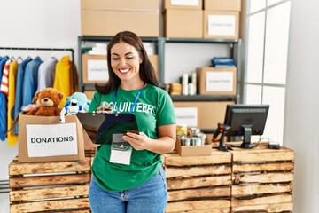 Young beautiful hispanic woman volunteer smiling confident writing on document at charity center