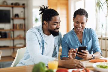 Happy African American couple using a phone while having breakfast in the morning.