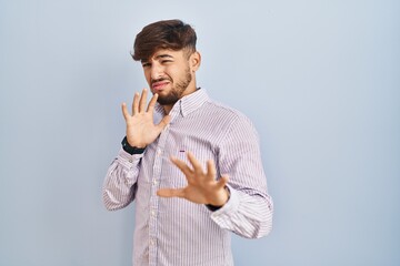 Arab man with beard standing over blue background disgusted expression, displeased and fearful...