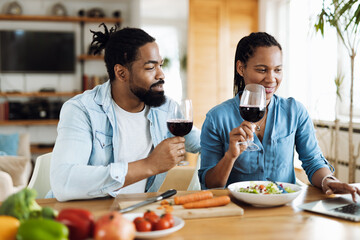 Young African American couple watching something on a computer while drinking wine together at home
