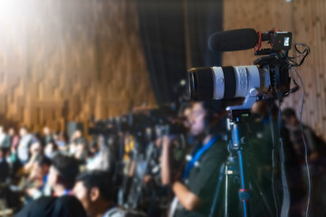 Press conference. Close-up of Video camera on blurred group of press and media photographer as...