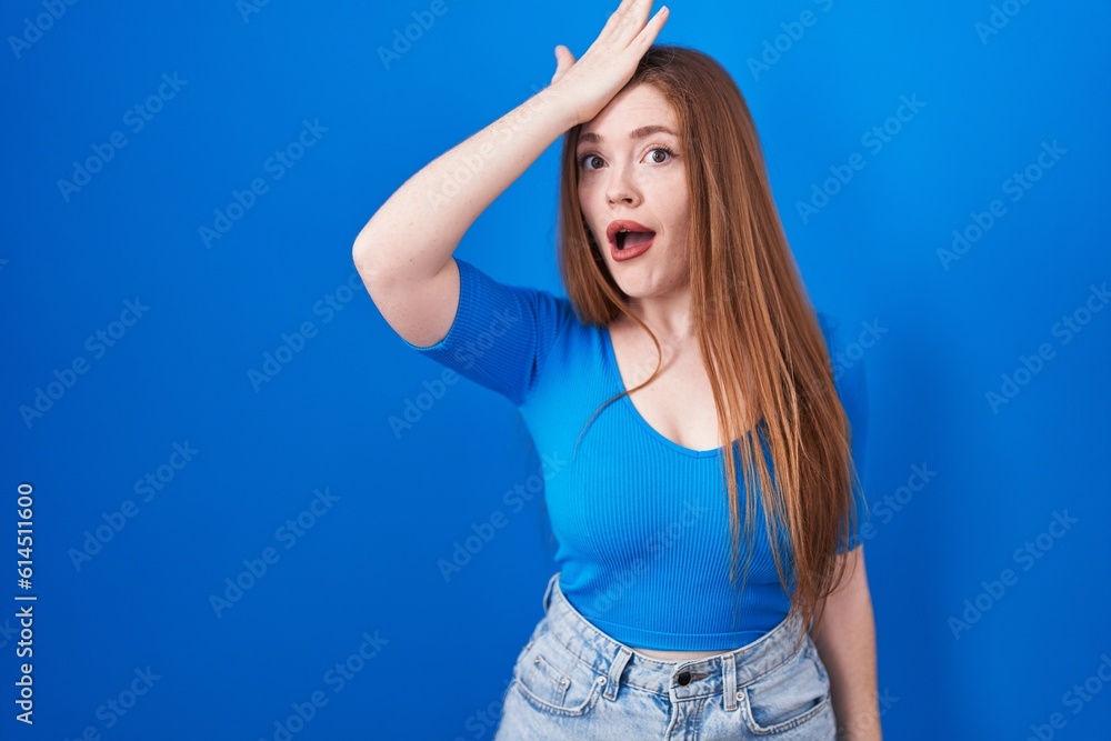 Sticker redhead woman standing over blue background surprised with hand on head for mistake, remember error.