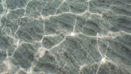 glare of sun plays on sandy bottom in shallow water. Top view on sandy seabed in shallow water with diagonal lines of sand and sun glare on its surface in brightly suny day, Red sea, Egypt