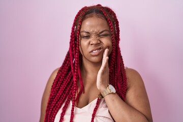 African american woman with braided hair standing over pink background touching mouth with hand with painful expression because of toothache or dental illness on teeth. dentist