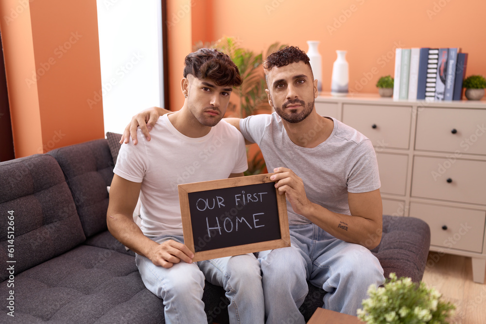 Wall mural Homosexual gay couple holding blackboard with first home text relaxed with serious expression on face. simple and natural looking at the camera.