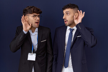 Two hispanic business men wearing business clothes smiling with hand over ear listening an hearing to rumor or gossip. deafness concept.