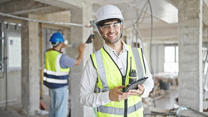 Two men builders smiling confident using touchpad at construction site