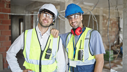 Two men builders smiling confident standing at construction site