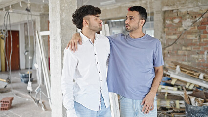 Two men couple hugging each other looking around at construction site