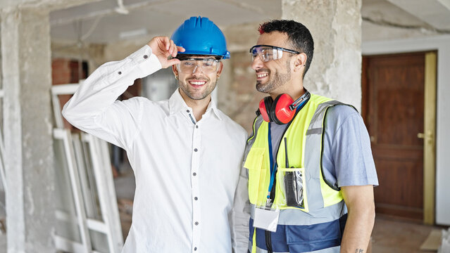 Two men builder and architect smiling confident standing together at construction site