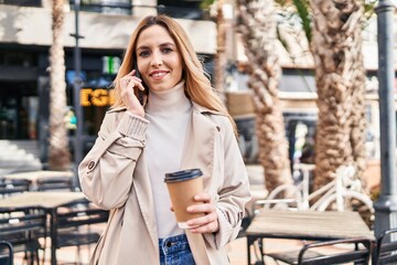 Young blonde woman talking on smartphone drinking coffee at coffee shop terrace