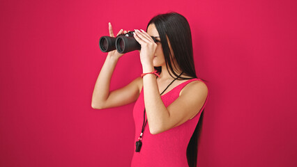 Young beautiful hispanic woman lifeguard using binoculars with relaxed expression over isolated red background