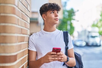 Young hispanic teenager student using smartphone with relaxed expression at street