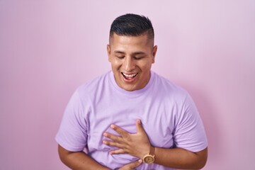 Young hispanic man standing over pink background smiling and laughing hard out loud because funny...