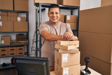 Young latin man ecommerce business worker leaning on packages at office
