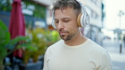 Young man listening to music with relaxed expression at street