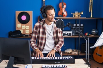 Fototapeta na wymiar Young hispanic man musician singing song playing piano at music studio