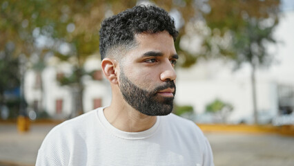 Young hispanic man looking to the side with serious expression at park