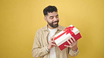 Young hispanic man smiling confident holding gift over isolated yellow background