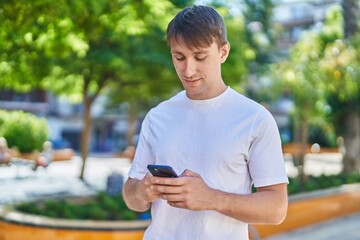 Young caucasian man using smartphone with serious expression at park