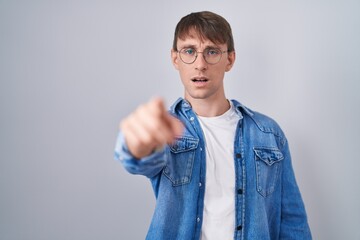 Caucasian blond man standing wearing glasses pointing displeased and frustrated to the camera,...