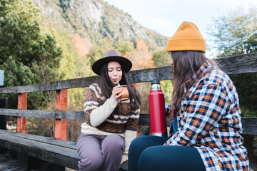 Two smiling young women friends enjoying and brewing yerba mate sitting on a rural scene