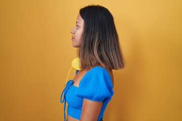 Hispanic young woman standing over yellow background looking to side, relax profile pose with...