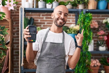 Middle age bald man working at florist shop holding dataphone smiling happy pointing with hand and finger to the side