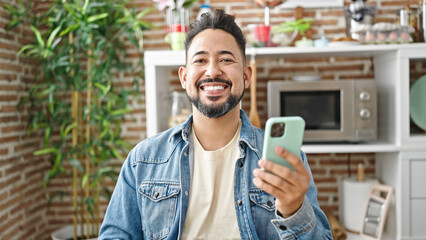 Young latin man using smartphones sitting on table at dinning room