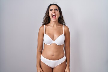 Fototapeta premium Young hispanic woman wearing white lingerie angry and mad screaming frustrated and furious, shouting with anger. rage and aggressive concept.
