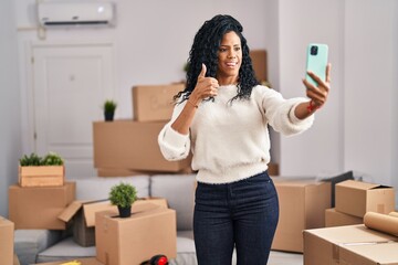 Obraz na płótnie Canvas Middle age hispanic woman moving to a new home taking selfie picture smiling happy and positive, thumb up doing excellent and approval sign