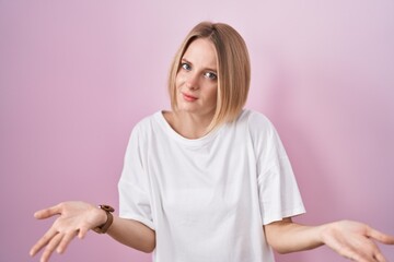 Obraz premium Young caucasian woman standing over pink background clueless and confused with open arms, no idea concept.