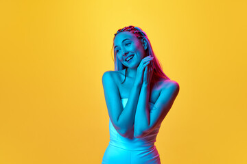 Happy, caring look. Portrait of attractive young woman with pretty, stylish hairstyle posing against yellow studio background in neon light. Concept of youth, emotions, beauty, lifestyle, ad