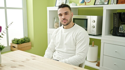 Fototapeta premium Young hispanic man sitting on table with serious expression at dinning room